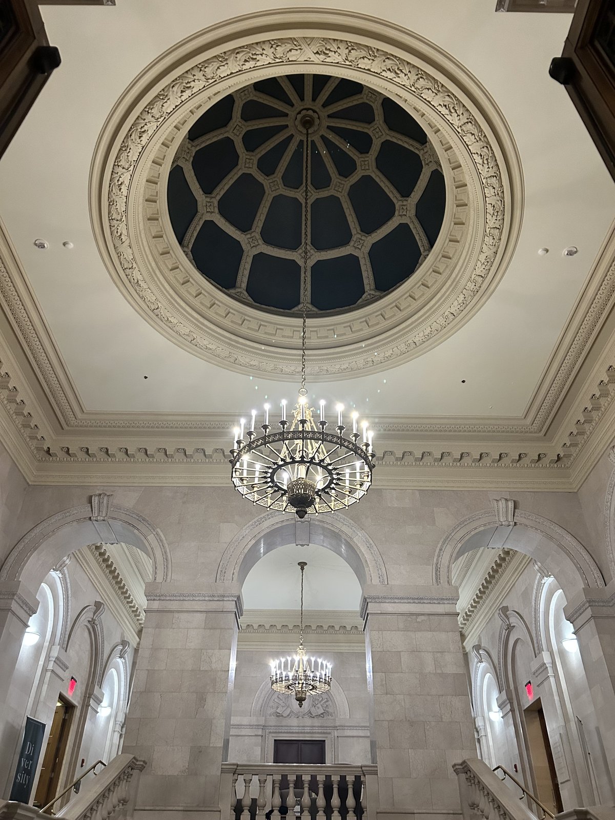 Looking straight up into a domed rotunda ceiling with a circular skylight and a chandelier